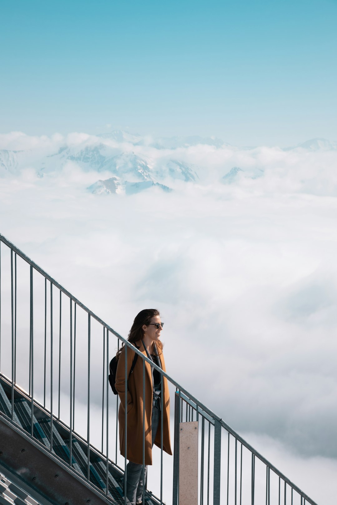 woman in brown tank top standing on black metal railings under white clouds during daytime