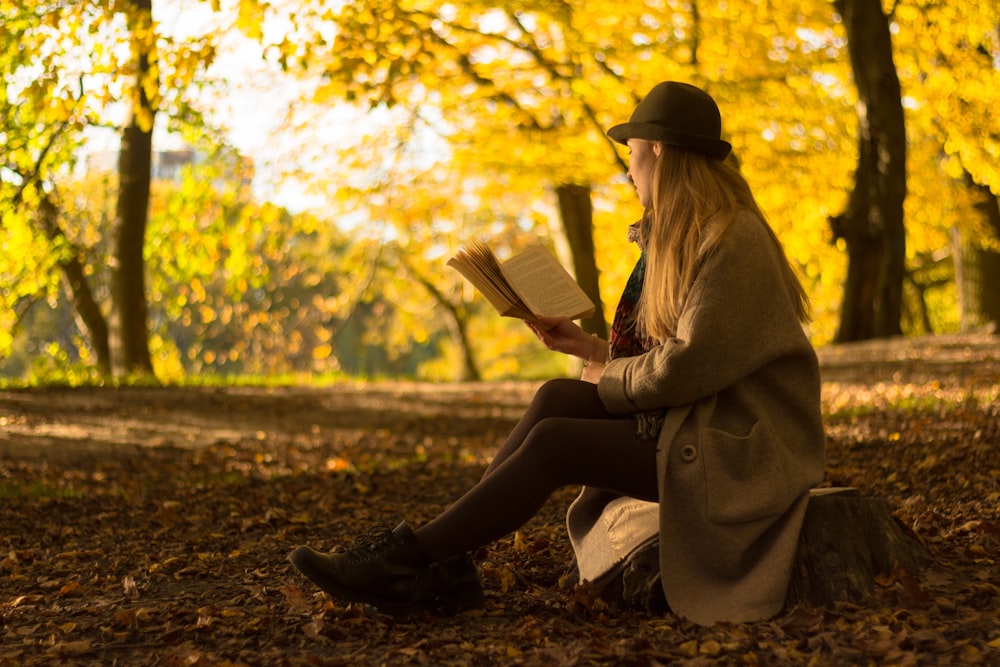 茶色のコートと黒い帽子をかぶった女性が、昼間、枯れ葉で地面に座っている