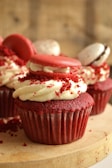 Freshly baked red velvet cupcakes with creamy white frosting and a sprinkle of red crumbs