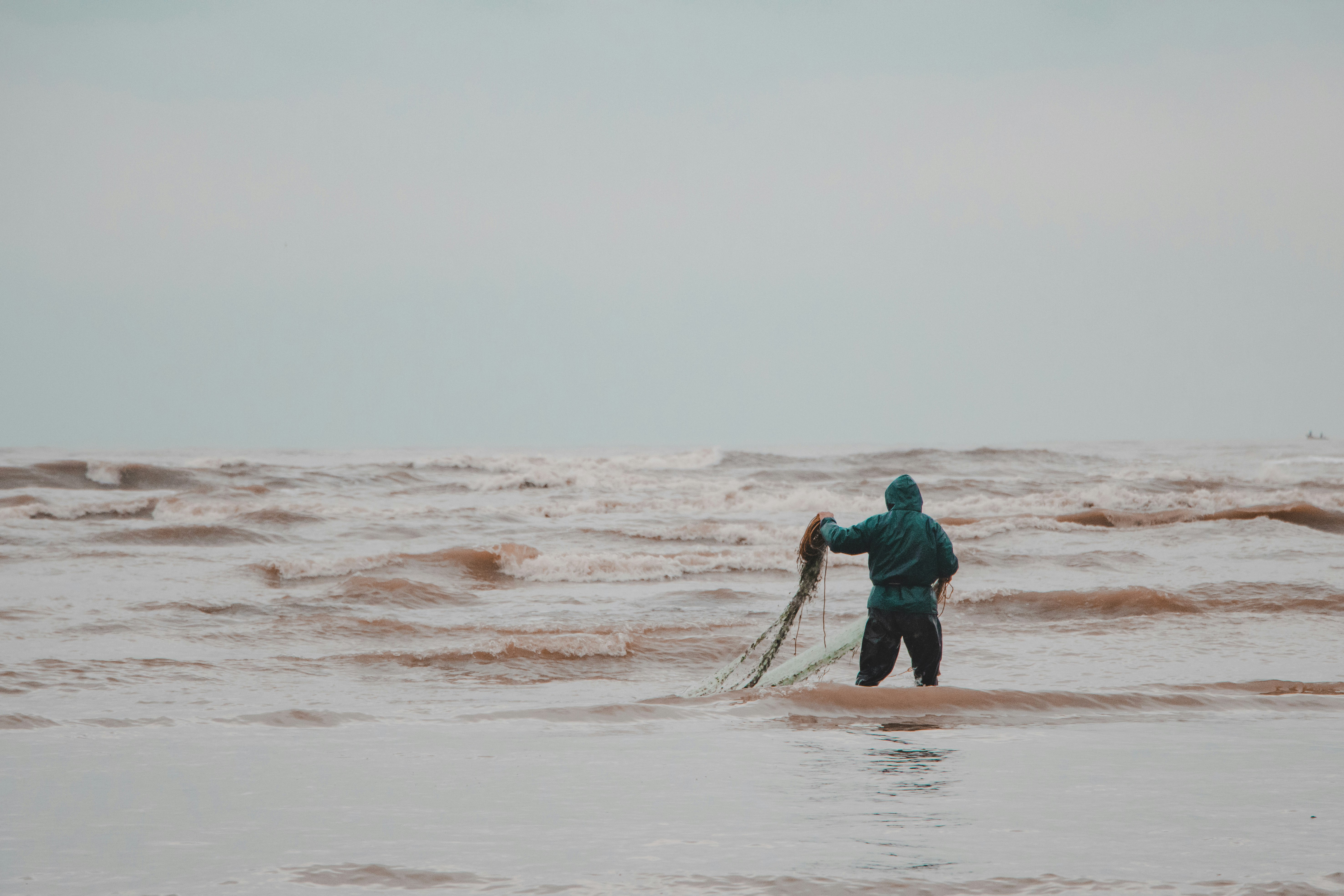 man in blue jacket and black pants walking on beach during daytime