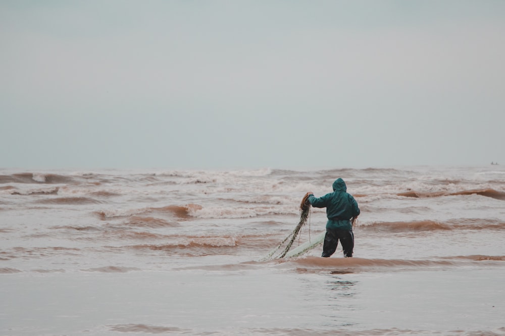 Mann in blauer Jacke und schwarzer Hose tagsüber am Strand spazieren