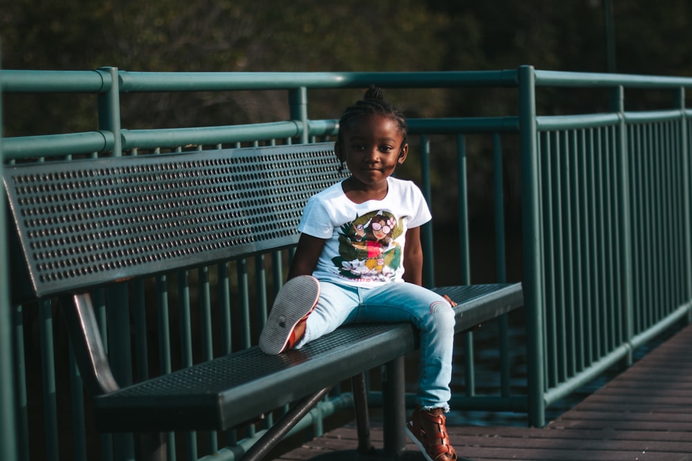 boy in white t-shirt sitting on brown wooden bench during daytime