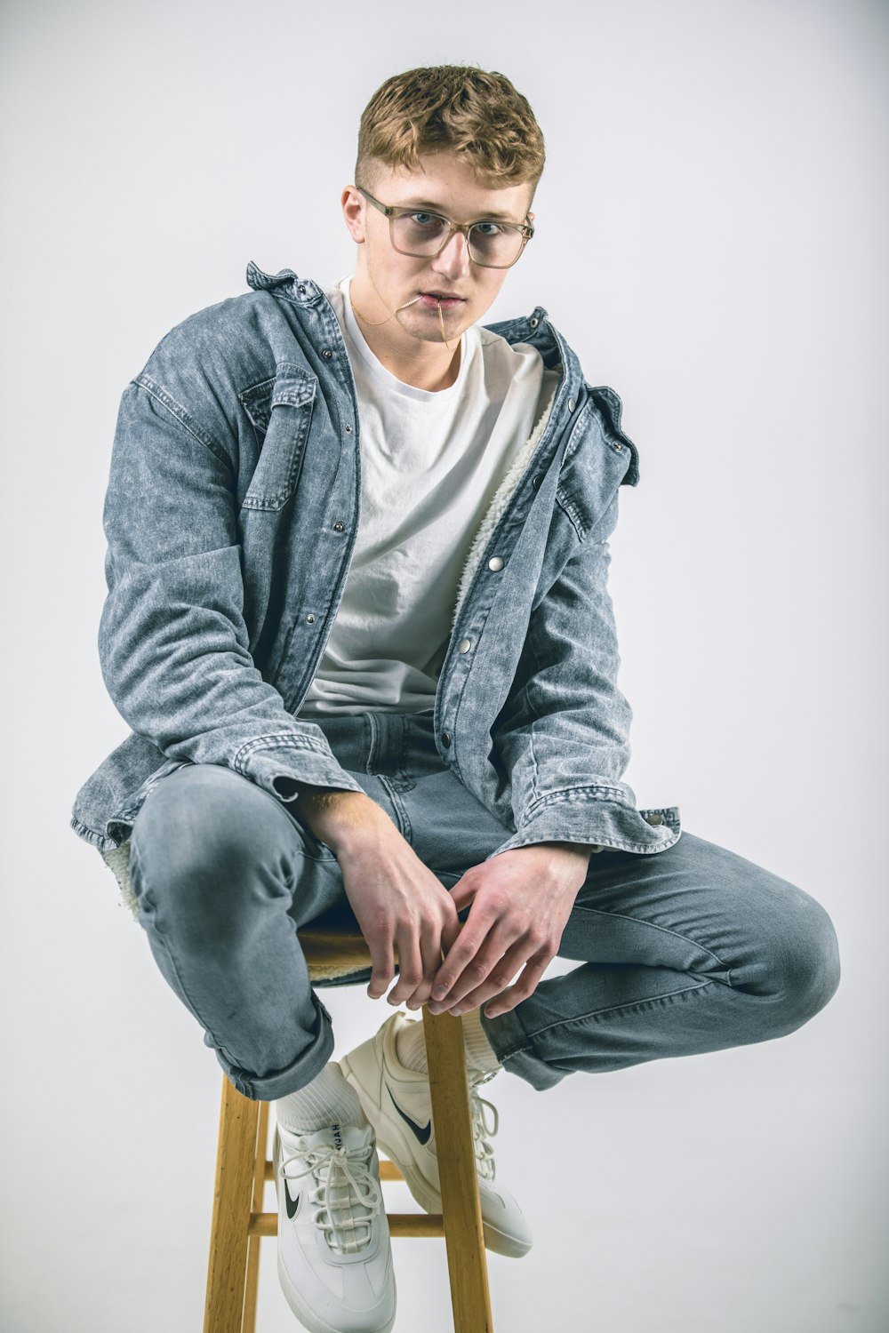 man in gray zip up jacket and gray denim jeans sitting on brown wooden seat