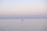 A lone individual engages in stand-up paddleboarding on a vast, calm, and peaceful body of water. The serene sky gradually transitions from soft pinks to pale blues, suggesting an early morning or late evening setting.