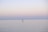 A lone individual engages in stand-up paddleboarding on a vast, calm, and peaceful body of water. The serene sky gradually transitions from soft pinks to pale blues, suggesting an early morning or late evening setting.