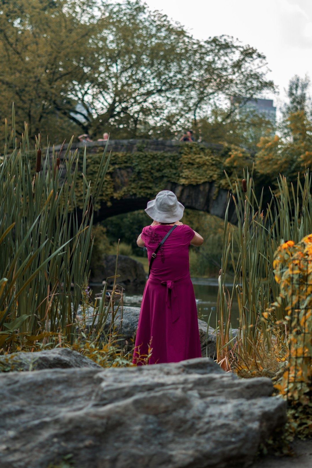 woman in purple dress standing on rock near green grass during daytime