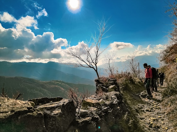 A vibrant photo of happy travelers exploring a scenic mountain trail under a clear blue sky.
