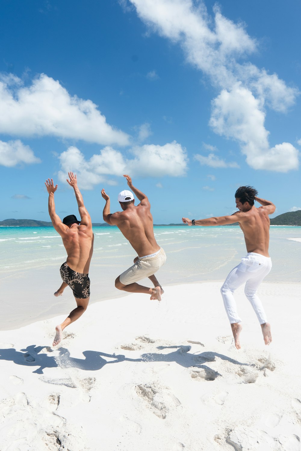 2 women in white shorts running on white sand beach during daytime