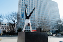 man in white shirt and black pants standing on black concrete bench near white building during