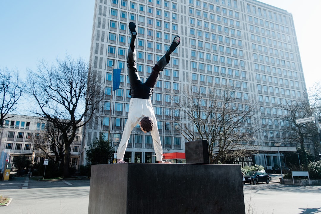 man in white shirt and black pants standing on black concrete bench near white building during