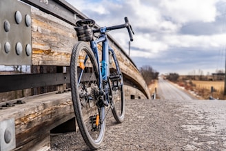 A rustic bicycle leaning against a weathered wooden fence with a vast open road stretching into the horizon under a soft sunset.