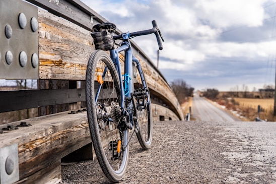 A rustic bicycle leaning against a weathered wooden fence with a vast open road stretching into the horizon under a soft sunset.