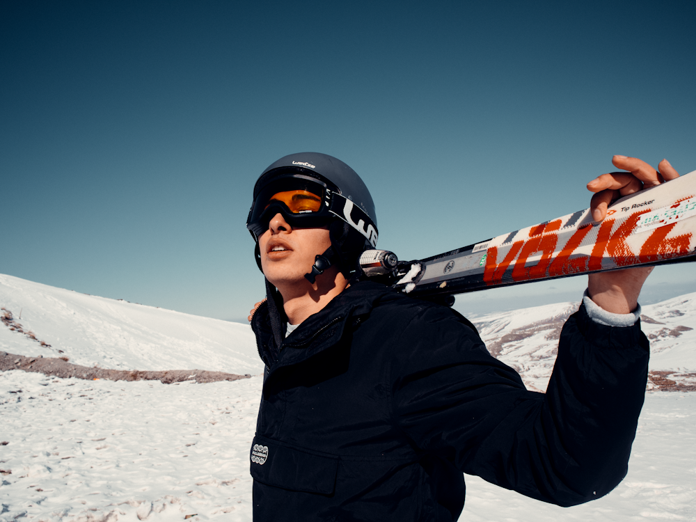 man in black jacket wearing black helmet and black goggles standing on snow covered ground during