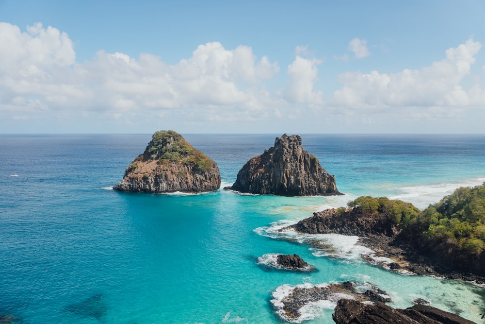 brown and green rock formation on blue sea under white clouds and blue sky during daytime