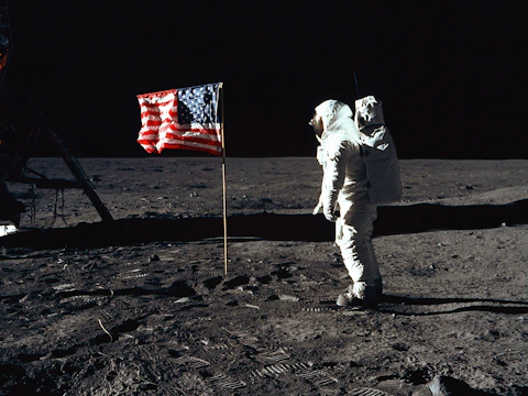 Silhouetted astronaut planting a flag on the lunar surface under a black sky.