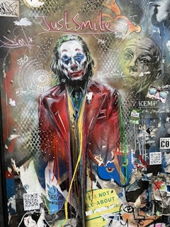 A performer in circus makeup standing beside a graffiti-covered wall with cryptic messages.