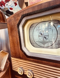 A vintage television set featuring a wooden frame and a black and white test pattern displayed on its screen. The image captures the details of the retro design, including the textured wood and intricate knobs. Part of a decorative colorful textile is visible in the background.