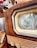 A vintage television set featuring a wooden frame and a black and white test pattern displayed on its screen. The image captures the details of the retro design, including the textured wood and intricate knobs. Part of a decorative colorful textile is visible in the background.