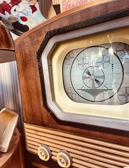 A vintage television set featuring a wooden frame and a black and white test pattern displayed on its screen. The image captures the details of the retro design, including the textured wood and intricate knobs. Part of a decorative colorful textile is visible in the background.