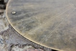 A close-up of a weathered metallic disk on a rocky surface, featuring engraved lines and text. The text includes names like 'BOYS PEAK' and 'MT. LIPIAH'. The disk appears to be part of a larger topographical or navigational instrument.