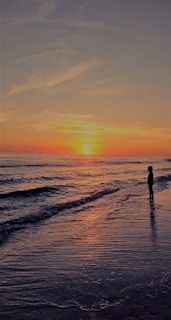 A vibrant sunset over a serene beach with a lone traveler gazing at the horizon.