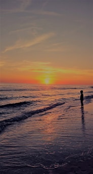 A vibrant sunset over a serene beach with a lone traveler gazing at the horizon.