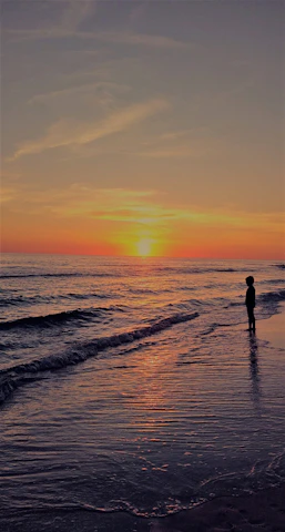 A serene beach sunset with a lone traveler gazing at the horizon, symbolizing peaceful journeys.