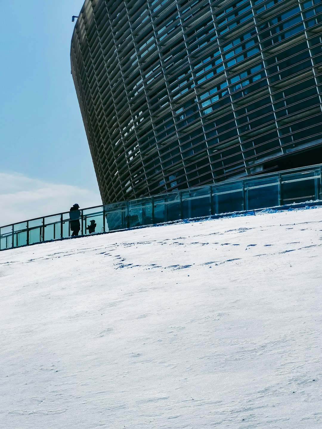 person walking on snow covered ground near glass building during daytime
