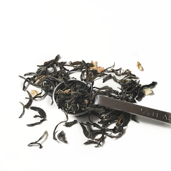 Loose-leaf tea spilling gently from a rustic wooden scoop onto a textured cloth.