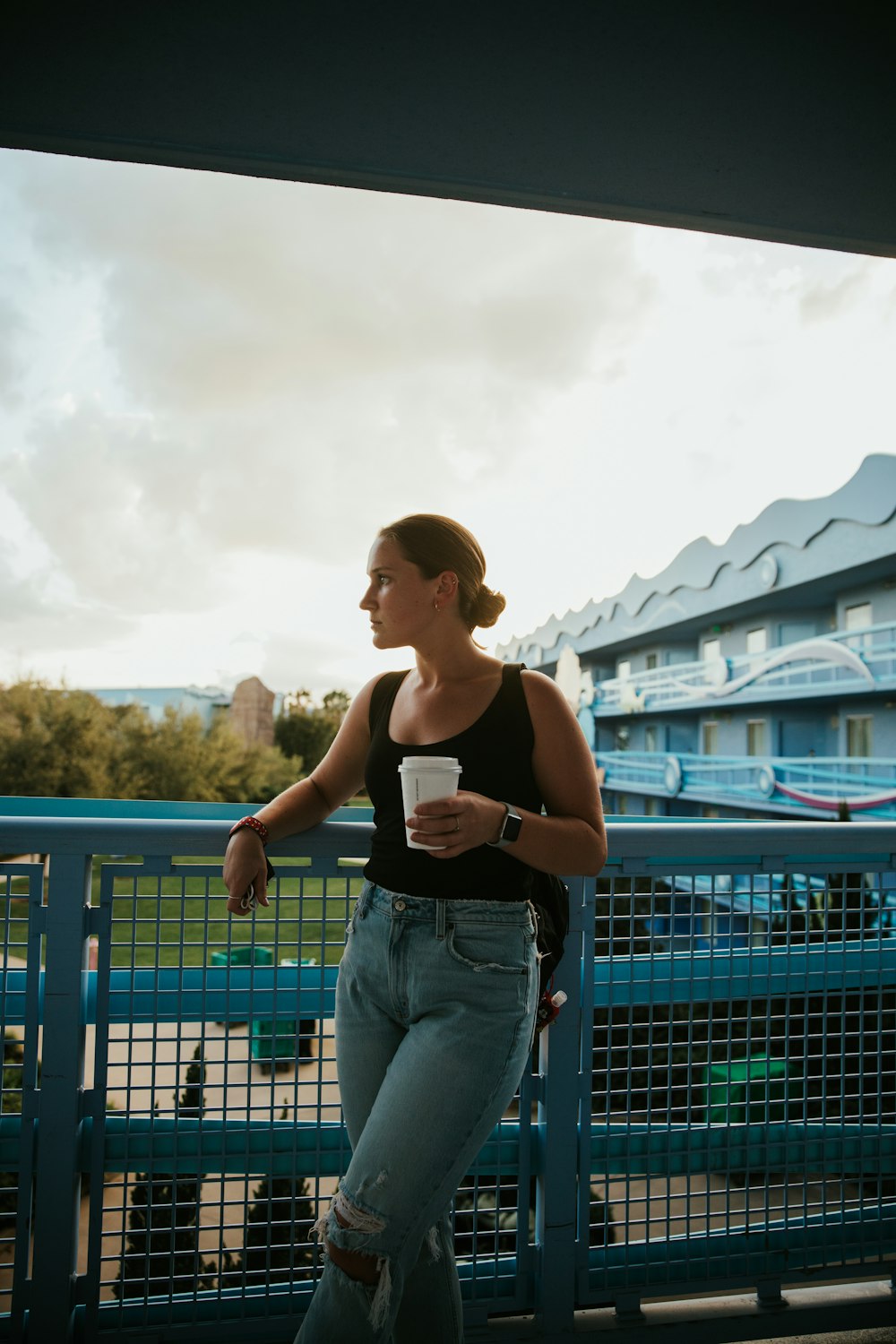 woman in black tank top and blue denim jeans standing near blue metal fence during daytime