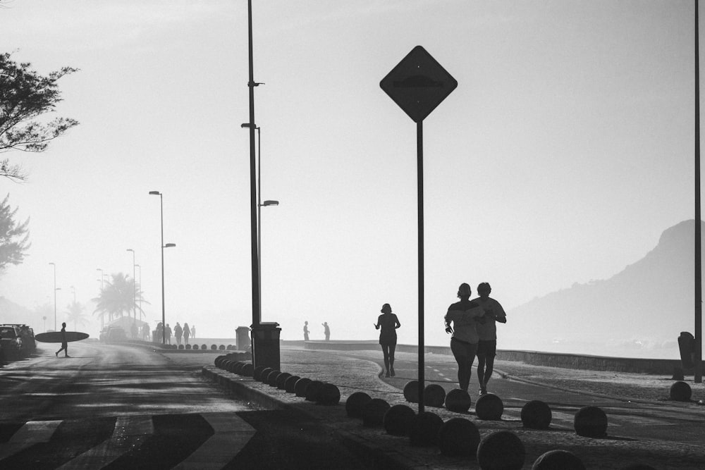 grayscale photo of people walking on sidewalk near body of water