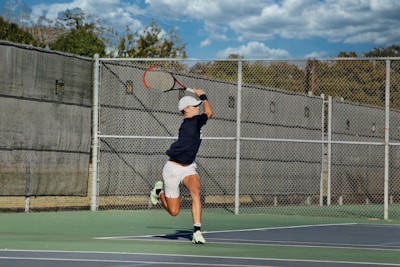 A tennis player stretching to return a fast serve on a sunny outdoor court.