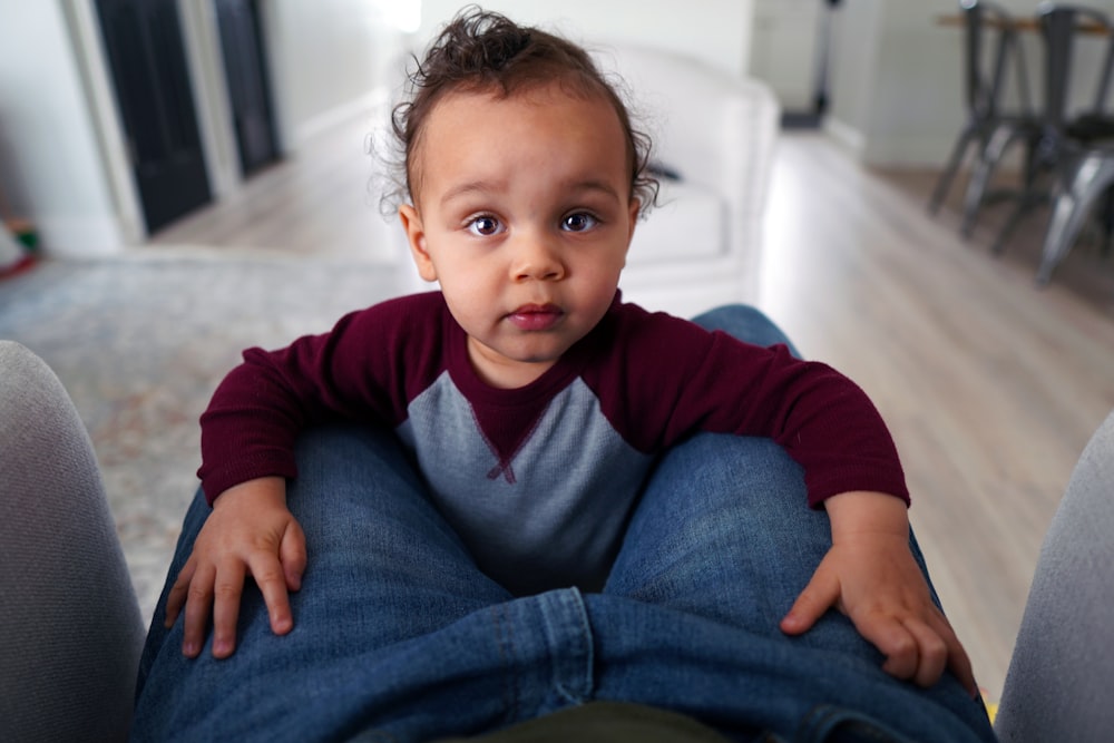 girl in red long sleeve shirt and blue denim jeans sitting on white bed