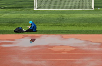 man in blue jacket and blue denim jeans sitting on green grass field during daytime