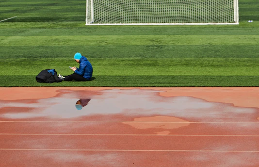man in blue jacket and blue denim jeans sitting on green grass field during daytime