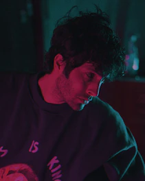 A moody, dark academia styled photo of Munir Khan reciting poetry under dim maroon lighting.