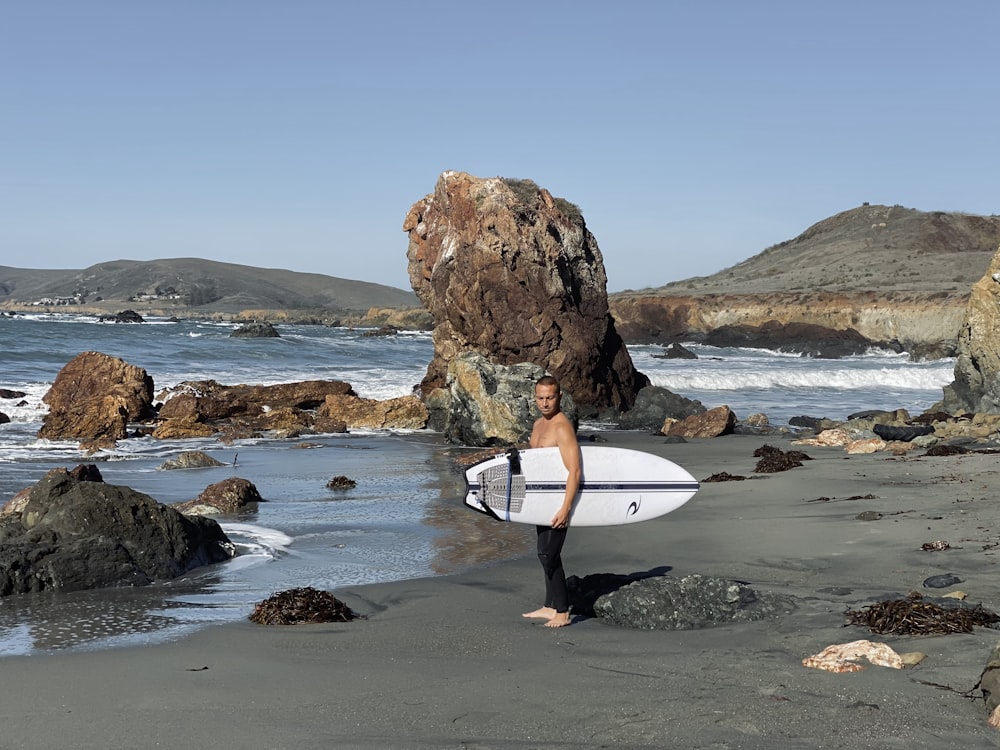 man in black wet suit holding white surfboard walking on seashore during daytime