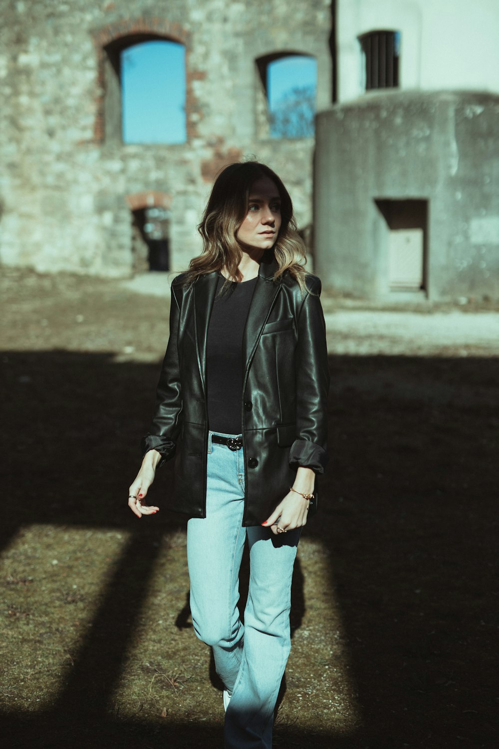 Frau in schwarzer Lederjacke und blauer Jeans tagsüber auf grauem Betonboden
