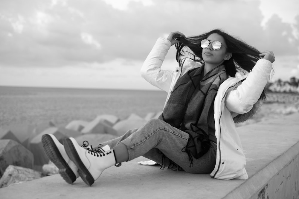 woman in white jacket and black pants sitting on beach shore