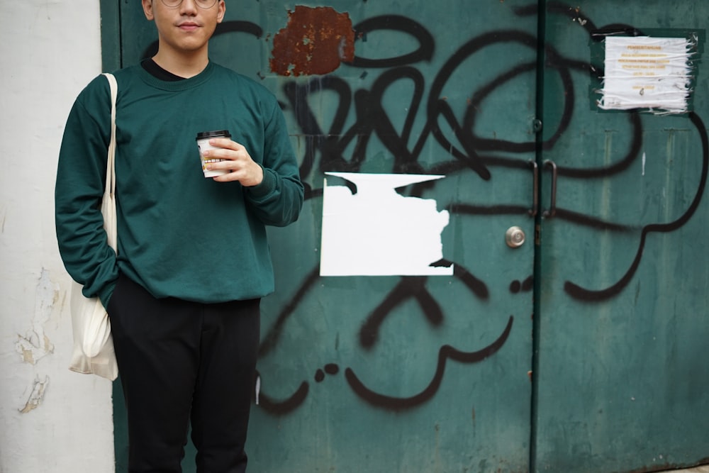 man in green sweater holding white printer paper standing beside black wooden door