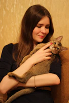 Tess smiling warmly while holding a contented cat after grooming.
