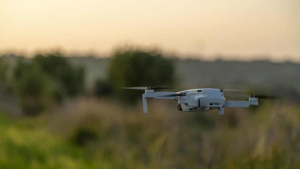 white drone flying over green grass field during daytime