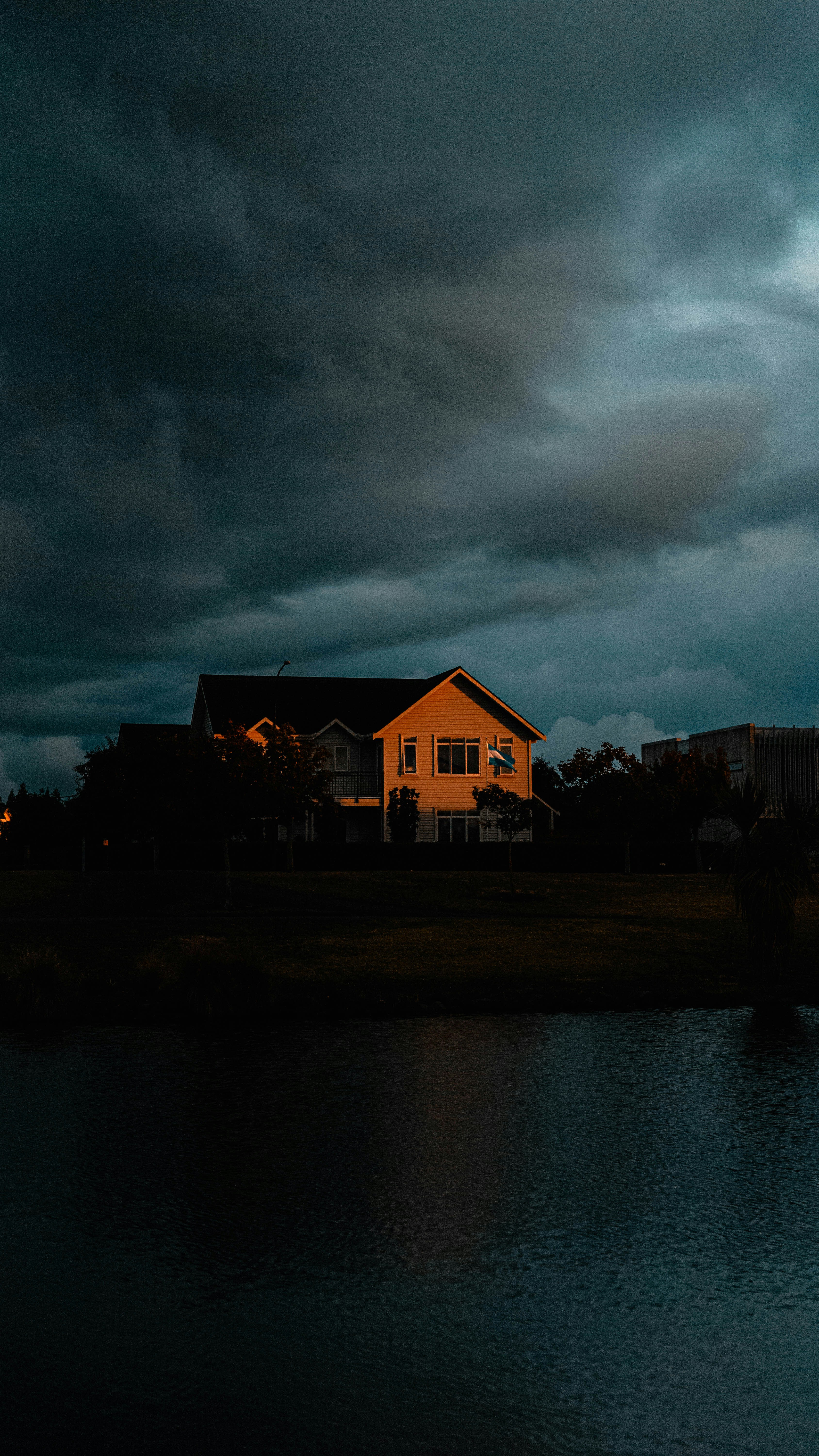brown and white house near body of water under gray clouds
