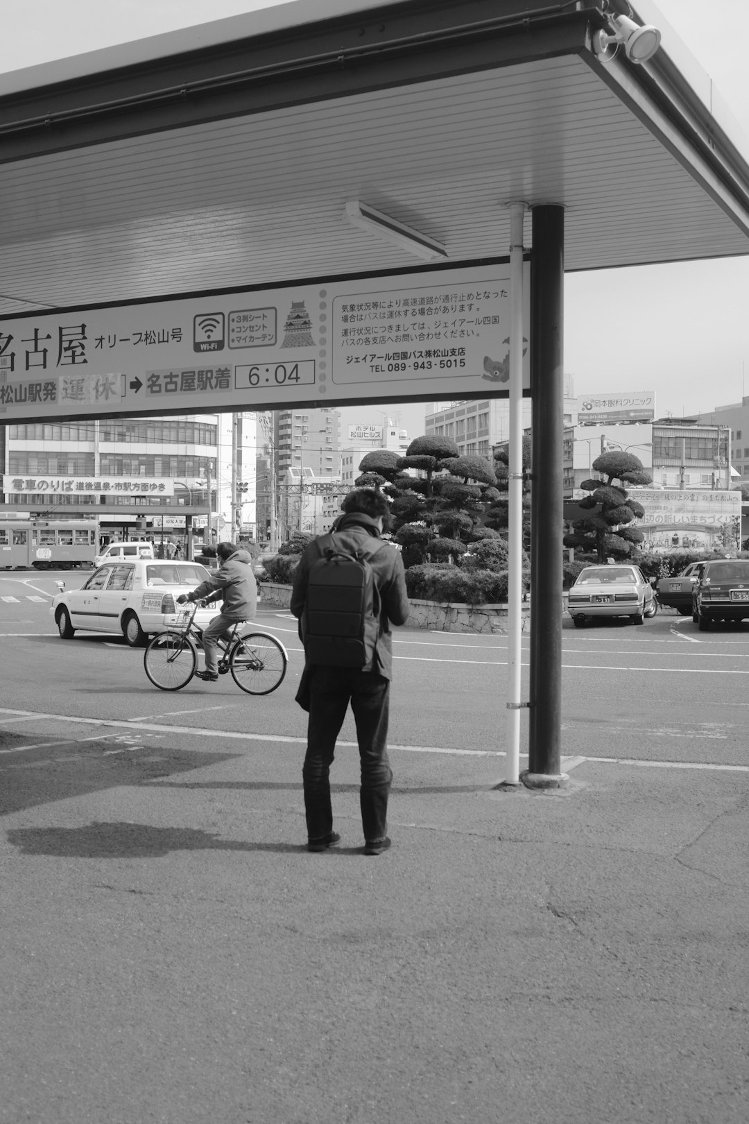 grayscale photo of man in black jacket and pants walking on sidewalk