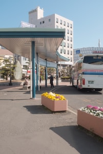 A modern bus parked at a city terminal with passengers boarding under a clear sky.