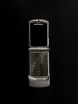 A silver Motorola flip phone is open and centered against a black background. The phone features a numeric keypad and a screen above it, with the brand name visible at the top.
