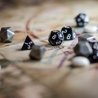 A collection of polyhedral dice scattered across a board game map, showcasing various shapes and numbers. The surface beneath the dice has intricate patterns and lines, indicating it is part of a role-playing game setup.