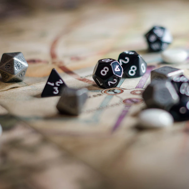 A collection of polyhedral dice scattered across a board game map, showcasing various shapes and numbers. The surface beneath the dice has intricate patterns and lines, indicating it is part of a role-playing game setup.