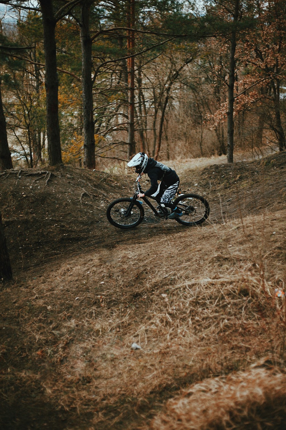흑인과 백인 재킷을 입은 남자가 낮 동안 숲에서 검은 산악 자전거를 타고 있습니다.