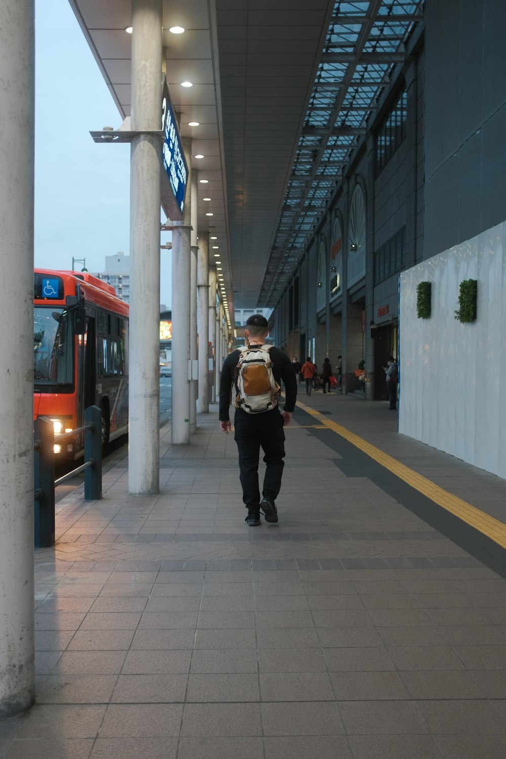 man in black jacket and black pants carrying backpack walking on sidewalk during daytime
